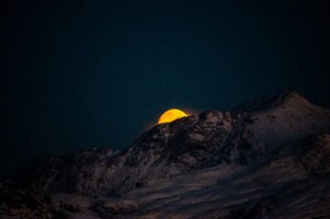 A near full moon is slowly creeping behind a mountain along the norwegian coast on an early winter morning near the town of Bodo.