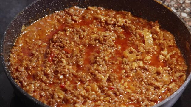 Close up view of cooked minced meat bolognese sauce with tomato base simmering in frying pan on stove, symbolizing homemade comfort food. Bo
