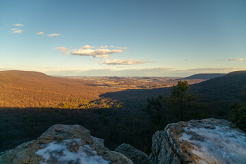 A view off a mountainside of the valley below with snow during the daytime. 