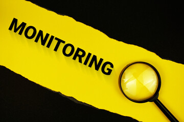 Monitoring text on yellow with black paper torn ripped and magnifying glass