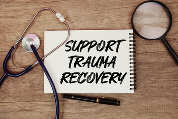 Support Trauma Recovery text written on notepad with stethoscope and magnifying glass on wooden background