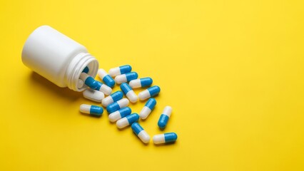 Blue and White Medicine Capsules Spilling Out of a White Plastic Bottle on Yellow Background