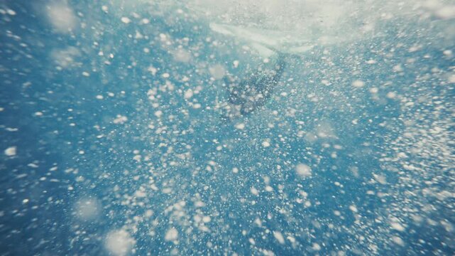 Humpback whale dives into deep ocean as bubbles and mist swirl underwater in slow motion