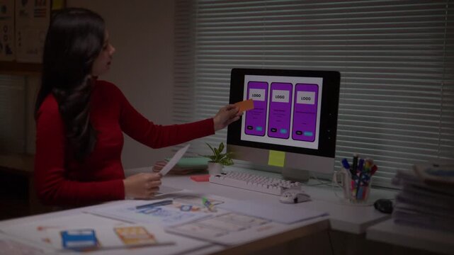 Young Asian woman working late at night, planning a mobile app. A creative UI developer designing the user experience for a smartphone