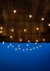 Conceptual romantic background of a cafe's ceiling with a lot of hanging light bulbs, and blue hour sky