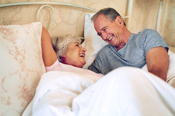 Senior couple, talk and laugh on bed in home with love, bonding and funny story in relationship....