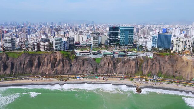 Sunny morning Miraflores Barranco Barranquito Playa Makaha beach pier aerial drone Lima Peru clear hazy blue skies cars traffic surf waves ocean seaside residential skyscraper buildings left motion