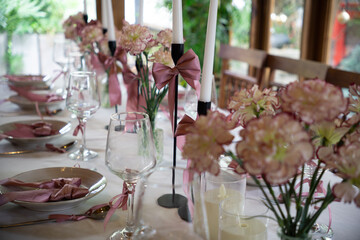 A beautifully set dining table adorned with pink flowers, ribbons, and elegant glassware, ready for...