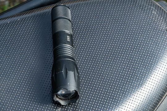 Black tactical flashlight with knurled grip and scalloped bezel placed on patterned surface