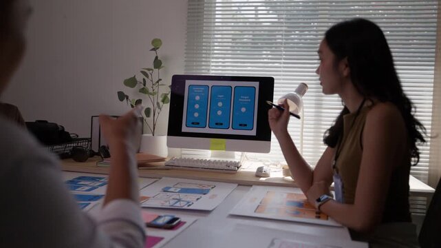 Creative female UX developer and UI designer collaborating on a mobile app interface, sharing ideas and working together in a modern office