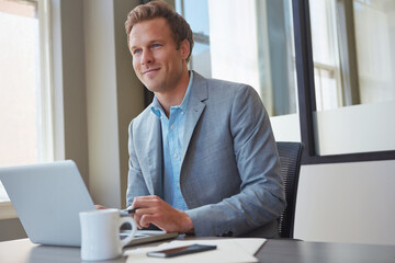 Fototapeta premium Businessman, thinking and laptop in office for finance, trading and smile for increase in market value. Trader, tech and opportunity in agency for crypto investment, account management or goal idea