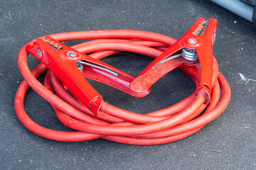 Red jumper cables with alligator clips coiled on dark surface for vehicle use