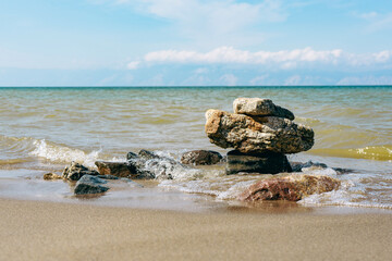 Rock formation on a sandy beach shore with calm ocean waves rolling in. Serene coastal landscape for travel and nature themes.