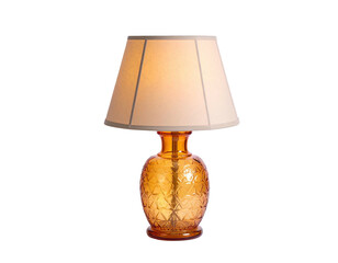 A classic amber-colored bedside lamp, illuminated. It has a patterned glass base and a cream shade