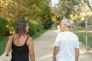 Obraz premium A man and a woman are walking together on a path. The man is wearing a white shirt and the woman is wearing a black tank top. They are both carrying handbags. Scene is casual and relaxed