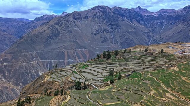 Reverse-moving drone pulls away from canyon edge to reveal layered terraced farmland as the full height and power of Colca Canyon&rsquo;s mountainscape emerges, including the dramatic opening of the canyon
