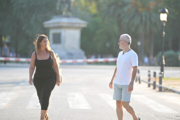 Fototapeta premium A man and a woman are walking down a street. The man is wearing a white shirt and shorts