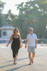 Fototapeta premium A man and a woman are walking down a street. The man is wearing a white shirt and shorts, while the woman is wearing a black dress. They are both smiling and seem to be enjoying their walk