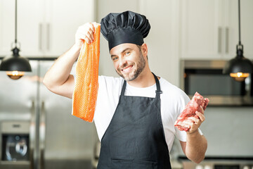 Health, natural protein concept. Handsome man in kitchen cooking fish and meat, salmon and beef in...