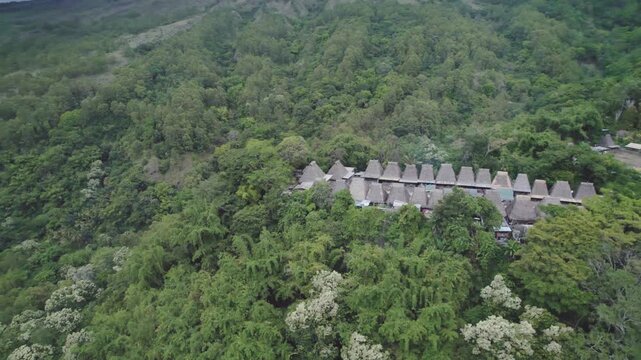 A cinematic drone orbiting shot of traditional thatched houses and megalithic structures in Bena Village, Flores, Indonesia.
