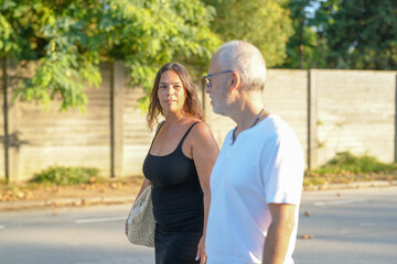 Obraz premium A man and a woman are walking down the street. The woman is wearing a black dress and the man is wearing a white shirt