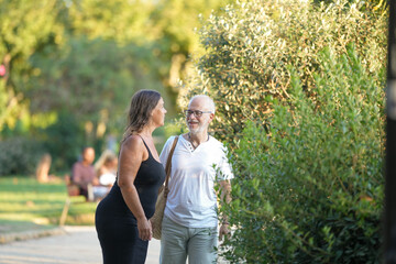 Obraz premium A man and a woman are walking in a park. The man is wearing a white shirt and jeans. The woman is wearing a black dress. They are both smiling and seem to be enjoying their time together