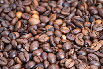 Naklejka premium Closeup dark roasted coffee beans piled with glossy oil sheen, deep brown tones, tight macro framing emphasizes texture and rich aroma for specialty roast marketing