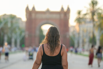 A woman with long hair is walking down a street in front of a large arch. The scene is bustling with people, and the woman is the center of attention