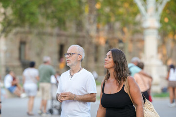 A man and a woman are walking in a crowded city street. The man is wearing a white shirt and glasses, while the woman is wearing a black tank top. They are both looking at something in the distance