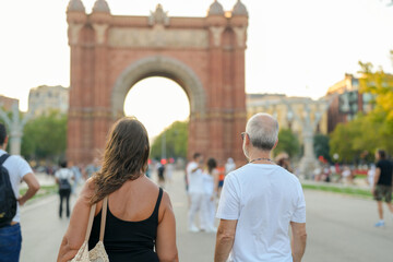A couple walking in front of a large archway. The woman is carrying a handbag. The man is wearing a white shirt