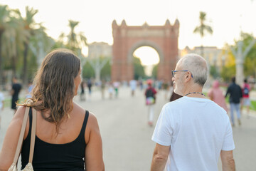 A man and a woman are walking down a street in a city. The man is wearing a white shirt and the woman is wearing a black tank top. They are both carrying handbags. The scene is lively