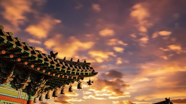 Ornate roof of a traditional structure adorned with multiple hanging bells and colorful patterns set against a vibrant sky with scattered orange clouds