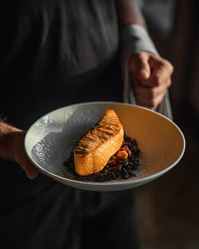 Grilled salmon fillet served by chef on dark background with elegant restaurant presentation