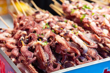Traditional Dongguan street food: grilled octopus tentacles on a barbecue grill, at a street food market in Dongguan City, Guangdong Province, China. © chuangxin