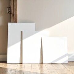Three blank white canvases lean against a light-filled wall