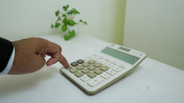 Person in a suit using a large calculator on a white surface