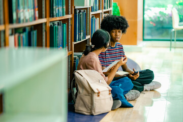 University students studying together between bookshelves showing group learning academic preparation self study routine knowledge development. © Wanwajee