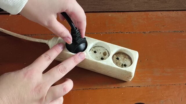 The hand unplugs the plug from the socket with an extension cord. electricity. Voltage, volts