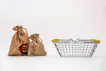 Two burlap bags labeled 'Risk' and a small shopping basket on a white background. The scene represents finance and shopping concepts.