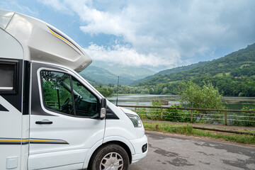 A motorhome parked next to a lake. The sky is cloudy, and the mountains in the background create a serene and peaceful atmosphere