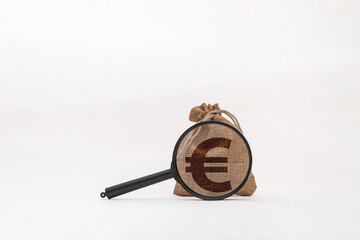 A burlap sack with a euro symbol printed on it, placed on a white background. A magnifying glass is positioned over the sack, emphasizing the currency symbol.