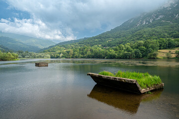 A lake with a boat and a small island in the middle. The water is calm and the sky is cloudy