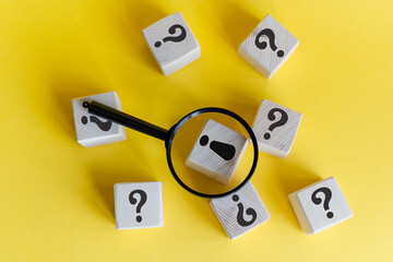 A magnifying glass focuses on a block with an exclamation mark, surrounded by blocks with question marks. The background is bright yellow, creating a vibrant contrast.