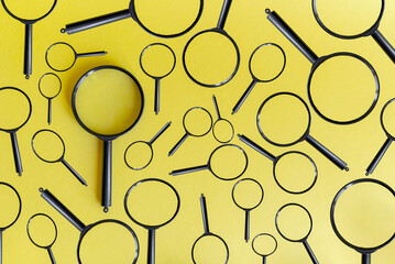 A collection of black magnifying glasses arranged on a bright yellow background. The scene features various sizes and orientations of the glasses.