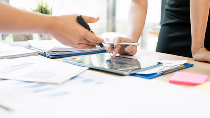 Close-up of business team analyzing financial data on a digital tablet and documents during a meeting in a modern office. Strategic planning and collaboration.