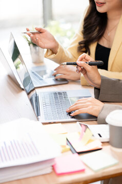 Two businesswomen's hands working on laptops, typing and analyzing paperwork charts in a meeting.