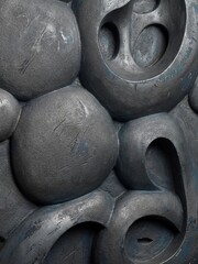 Small surface scratches mark the charcoal gray surface of this bulbous and porous relief sculpture.