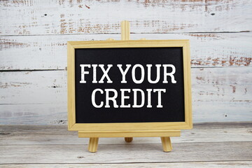Fix Your Credit text written on blackboard with alarm clock on wooden background