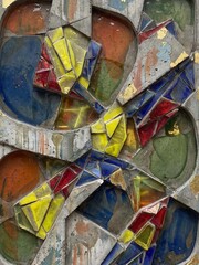 Textured grey cement contrasts sharply with fractured shards of primary colored glass and gold leaf.