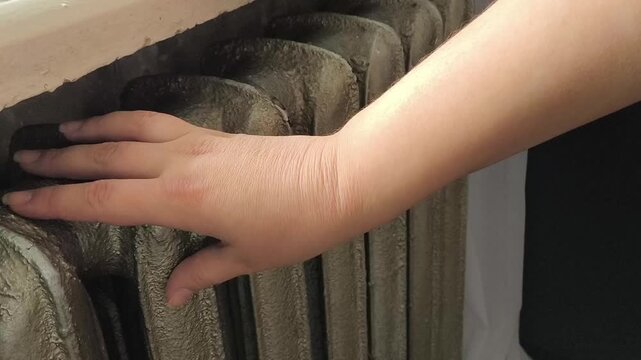 A woman warms her hands near an old heating radiator in the house. Old cast iron radiators in the house